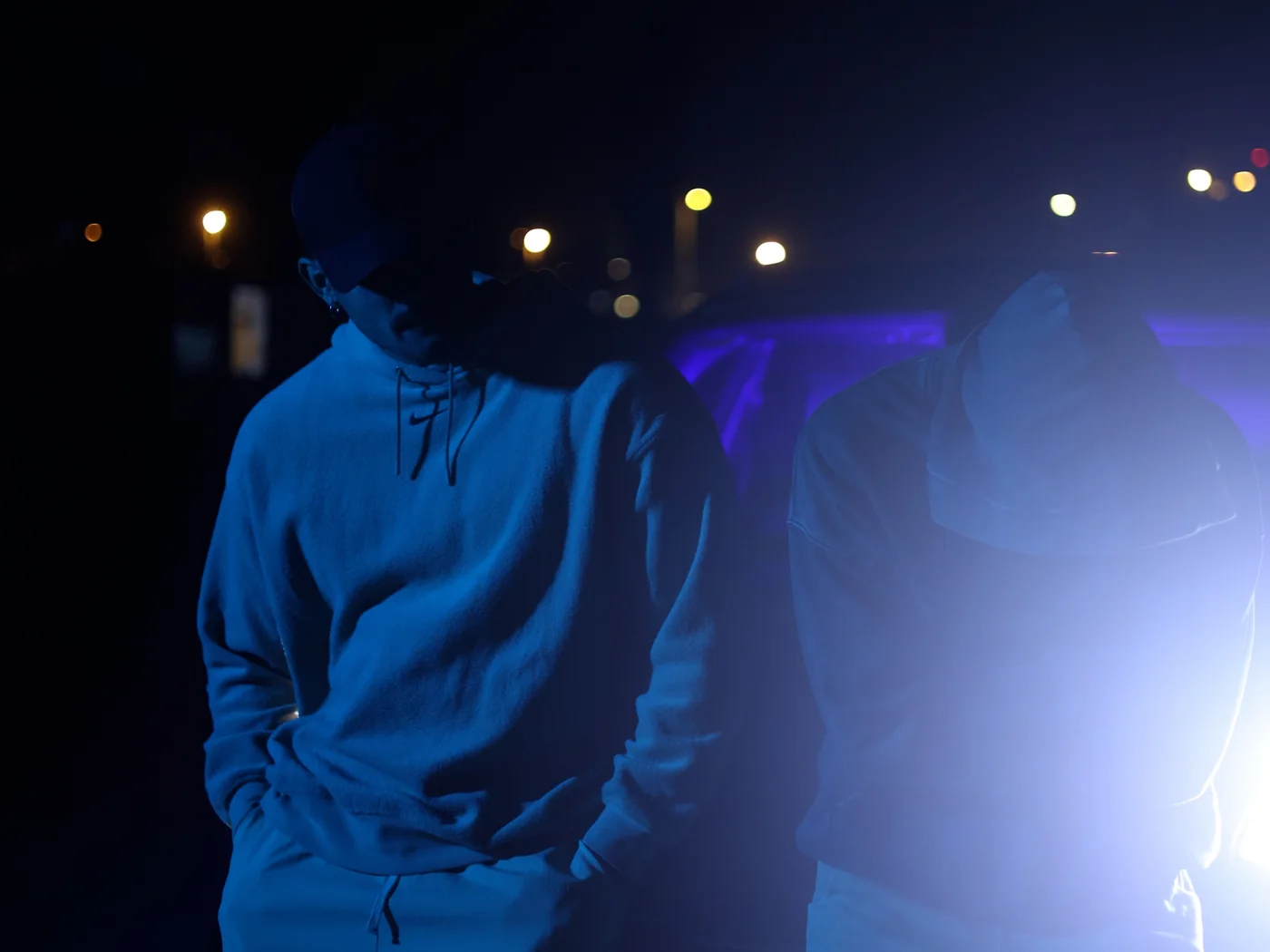 Dos artistas de noche bajo la luz azul de un coche