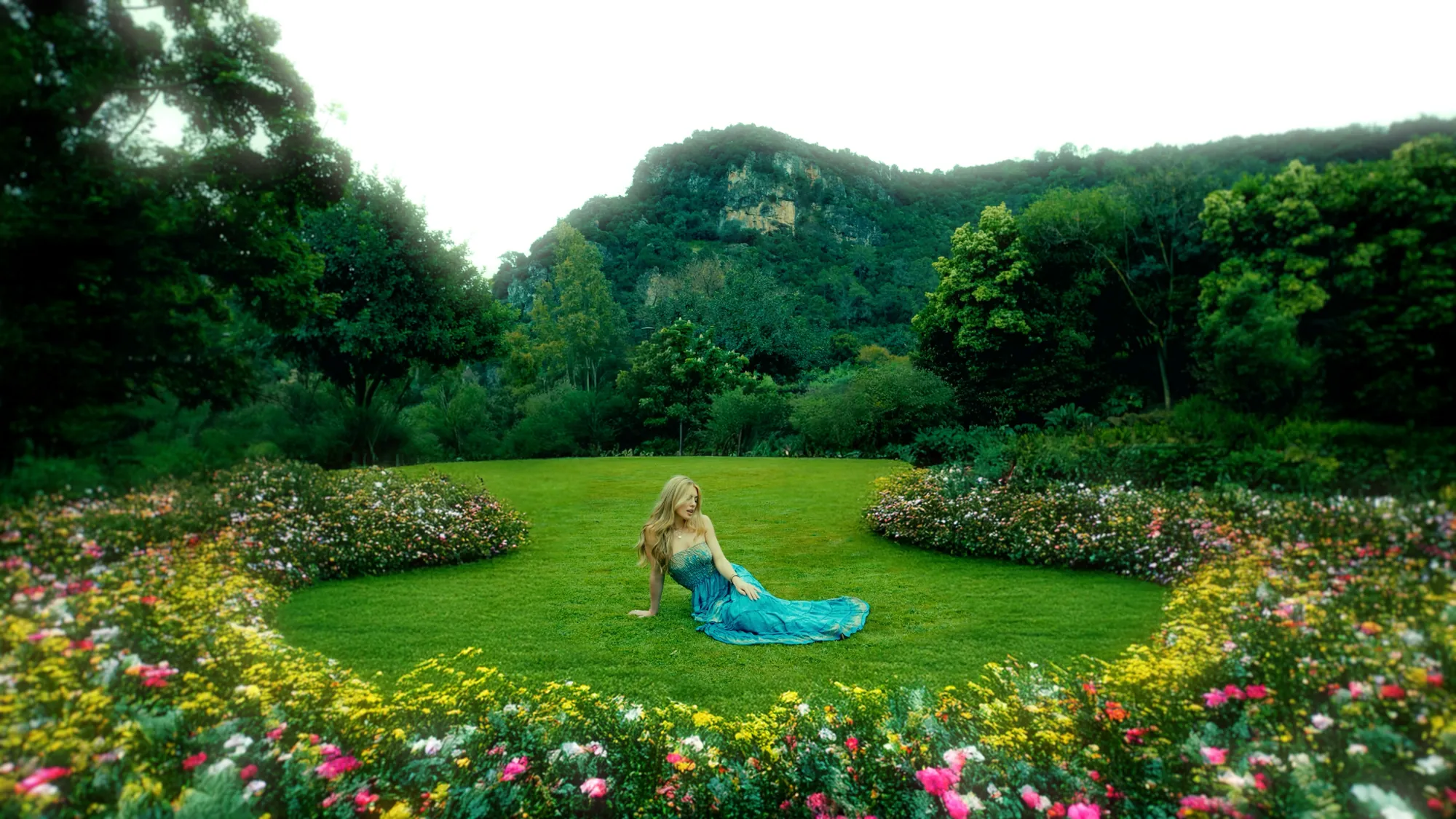Artista con vestido azul sentada en el césped de un jardín con flores